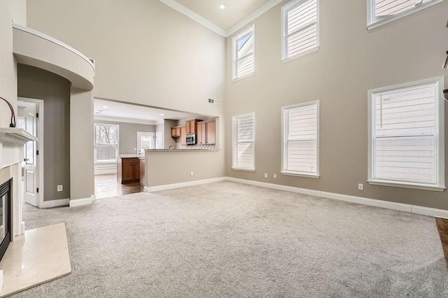 unfurnished living room featuring baseboards, light colored carpet, ornamental molding, a high ceiling, and a fireplace