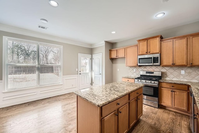 kitchen featuring light wood finished floors, visible vents, appliances with stainless steel finishes, a center island, and light stone countertops