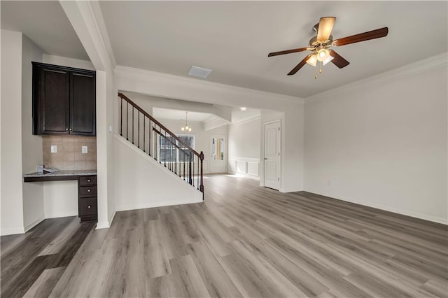 unfurnished living room with ceiling fan with notable chandelier, wood finished floors, and crown molding