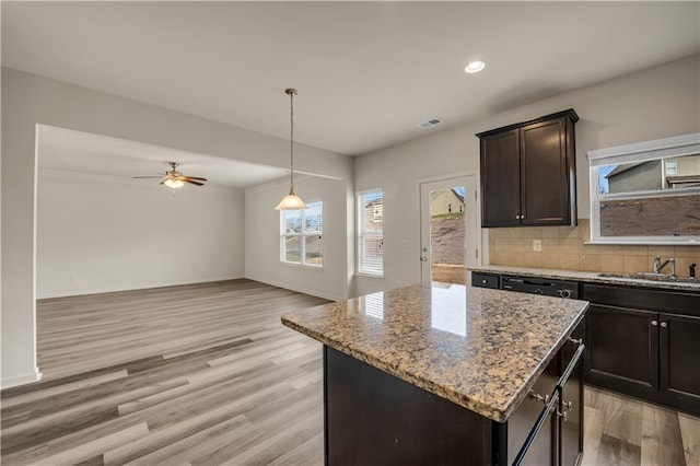 kitchen featuring light stone counters, light wood-type flooring, a kitchen island, and backsplash