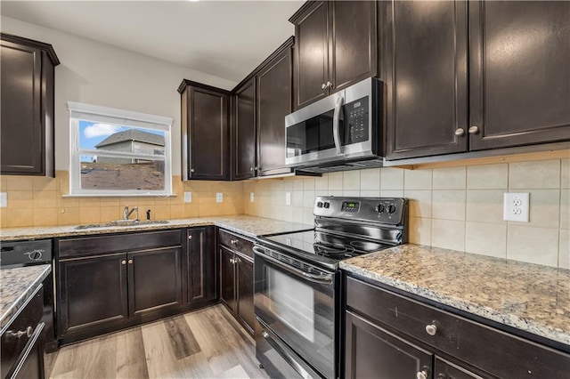 kitchen with light wood finished floors, stainless steel microwave, light stone counters, black range with electric stovetop, and a sink