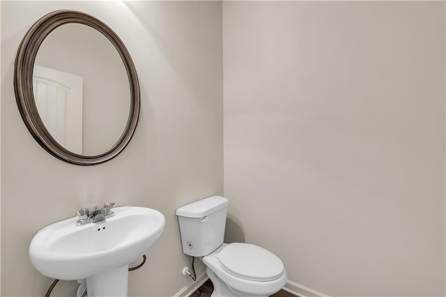 half bath featuring toilet, baseboards, and a sink