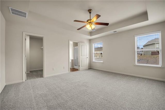 unfurnished bedroom with baseboards, visible vents, a raised ceiling, carpet, and a walk in closet