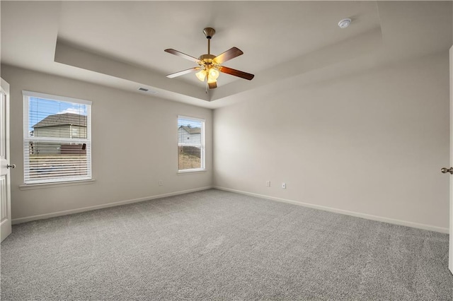 carpeted empty room featuring a raised ceiling, visible vents, ceiling fan, and baseboards