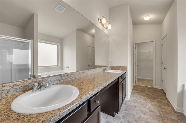 full bath featuring a stall shower, a walk in closet, visible vents, and a sink