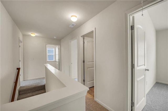 corridor featuring baseboards, attic access, visible vents, and light colored carpet