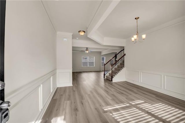 interior space featuring light wood-style flooring, ornamental molding, an inviting chandelier, stairs, and a decorative wall