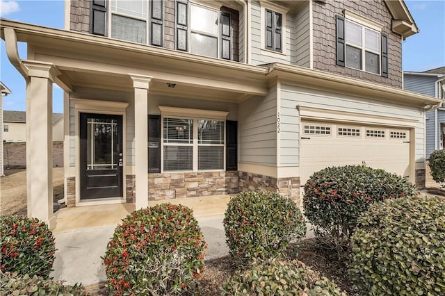 view of exterior entry featuring covered porch, stone siding, and an attached garage