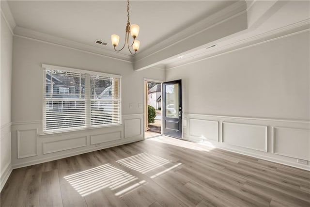 empty room featuring ornamental molding, visible vents, a notable chandelier, and wood finished floors