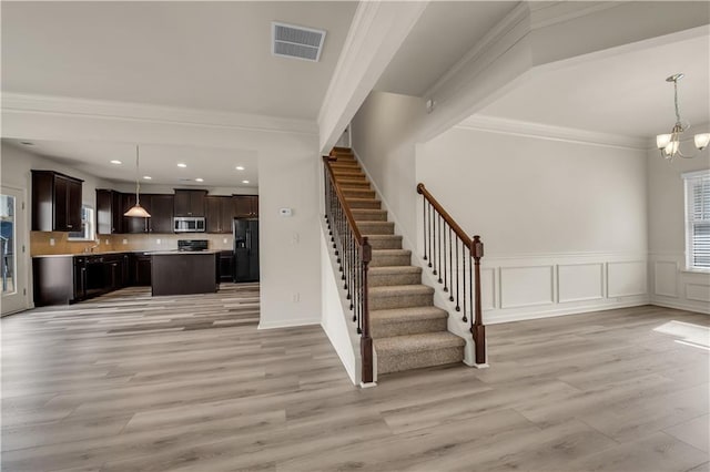 interior space with a chandelier, light wood-style flooring, visible vents, stairs, and crown molding