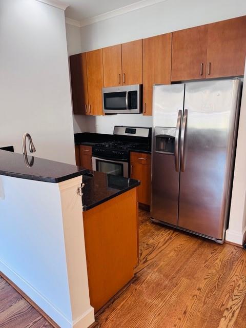 384 Ralph Mcgill Blvd NE Unit 121, Atlanta, GA 30312 - kitchen with stainless steel appliances, dark countertops, wood finished floors, brown cabinets, and ornamental molding