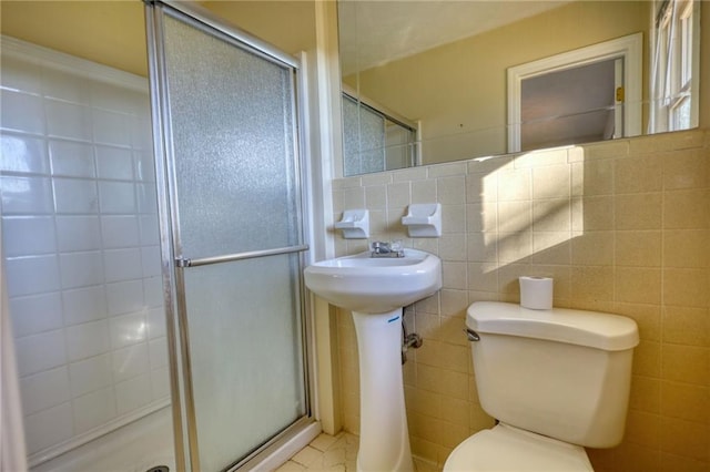 full bath with toilet, a stall shower, and tile walls