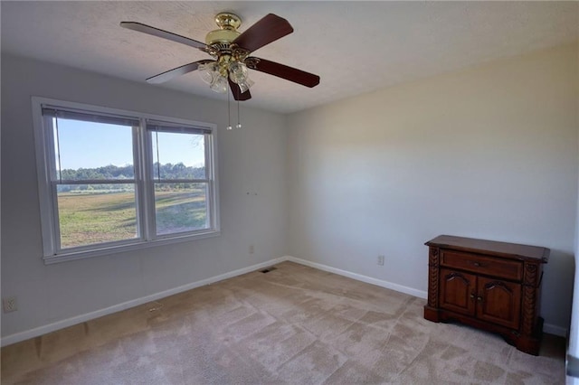 spare room featuring light carpet, visible vents, baseboards, and a ceiling fan