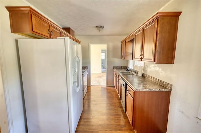 kitchen with light wood-type flooring, white appliances, brown cabinets, and a sink