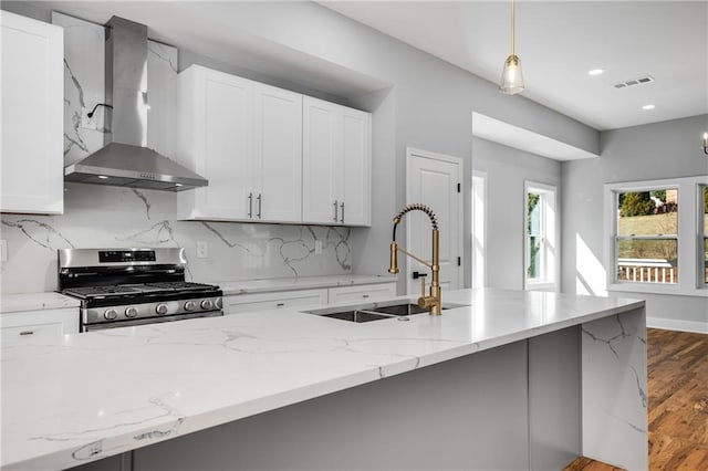 kitchen featuring dark wood-style flooring, a sink, wall chimney range hood, stainless steel gas stove, and backsplash