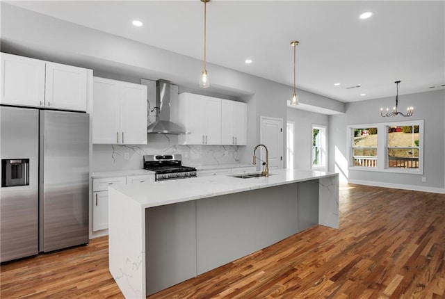 kitchen featuring decorative backsplash, appliances with stainless steel finishes, white cabinets, wall chimney exhaust hood, and a sink