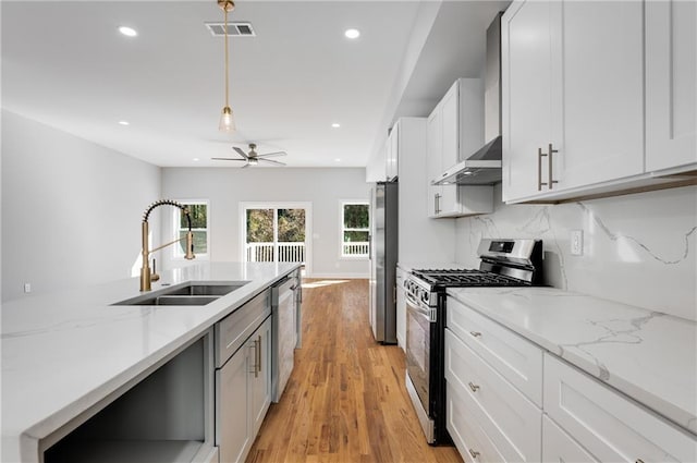 kitchen with visible vents, light wood finished floors, a sink, stainless steel appliances, and wall chimney range hood