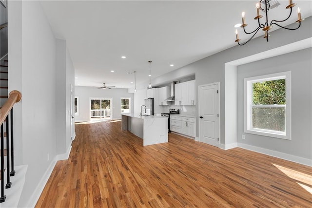 kitchen featuring wall chimney range hood, open floor plan, white cabinetry, stainless steel appliances, and light wood finished floors