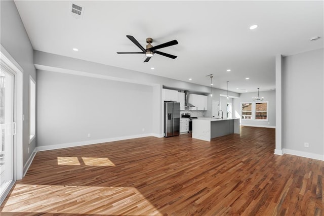 unfurnished living room featuring recessed lighting, ceiling fan with notable chandelier, dark wood-type flooring, and a sink