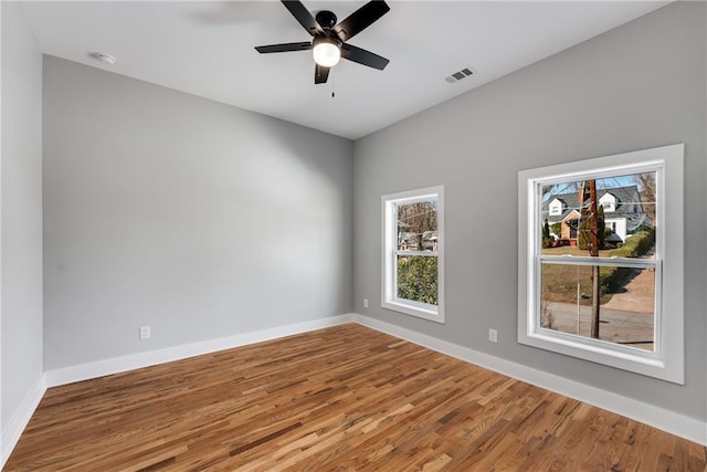 empty room with visible vents, ceiling fan, baseboards, and wood finished floors