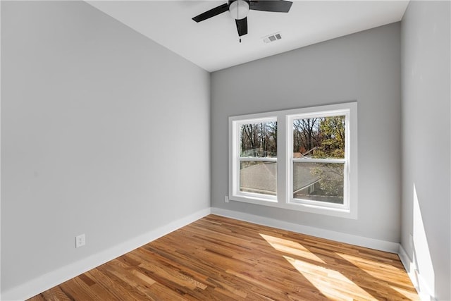 spare room with ceiling fan, visible vents, baseboards, and wood finished floors