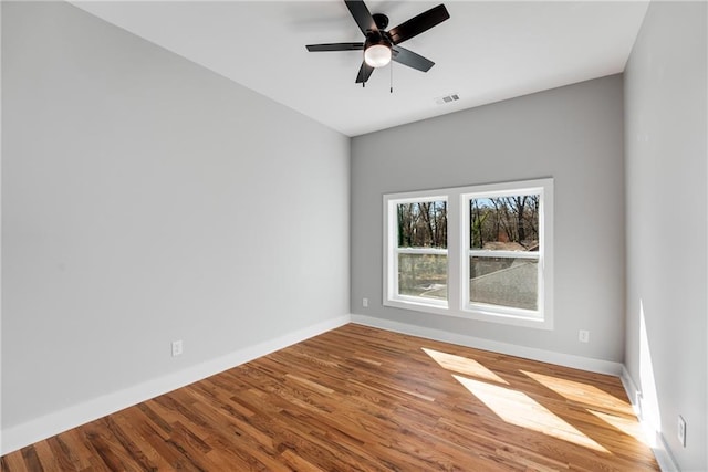 empty room featuring visible vents, a ceiling fan, baseboards, and wood finished floors