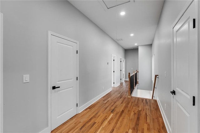 corridor with visible vents, baseboards, attic access, light wood-style floors, and an upstairs landing