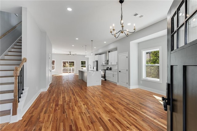 kitchen featuring visible vents, stainless steel appliances, white cabinets, wall chimney range hood, and open floor plan