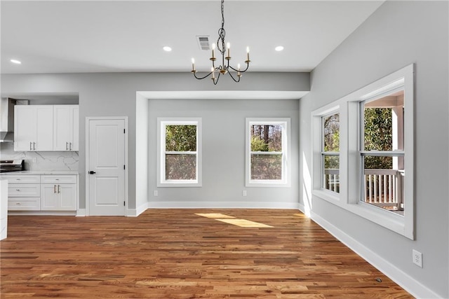 unfurnished dining area with wood finished floors, visible vents, baseboards, recessed lighting, and a chandelier