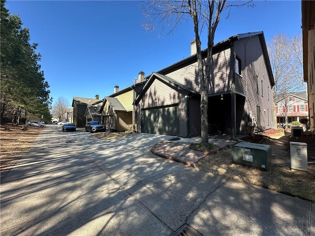 view of property exterior with a garage, a residential view, a chimney, and driveway