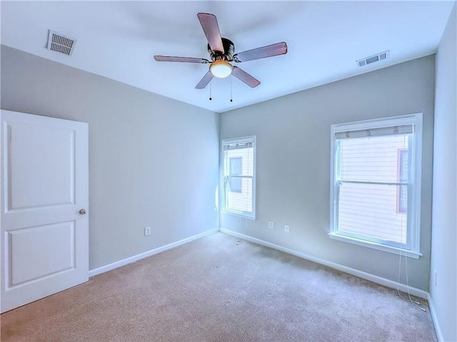 carpeted spare room featuring baseboards, visible vents, and ceiling fan