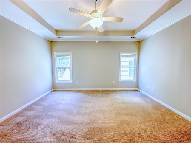 carpeted empty room featuring a ceiling fan, a tray ceiling, crown molding, and baseboards