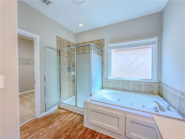 full bath featuring a spacious closet, visible vents, a whirlpool tub, a stall shower, and wood finished floors