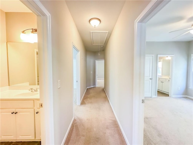 hall featuring a sink, baseboards, light colored carpet, and attic access