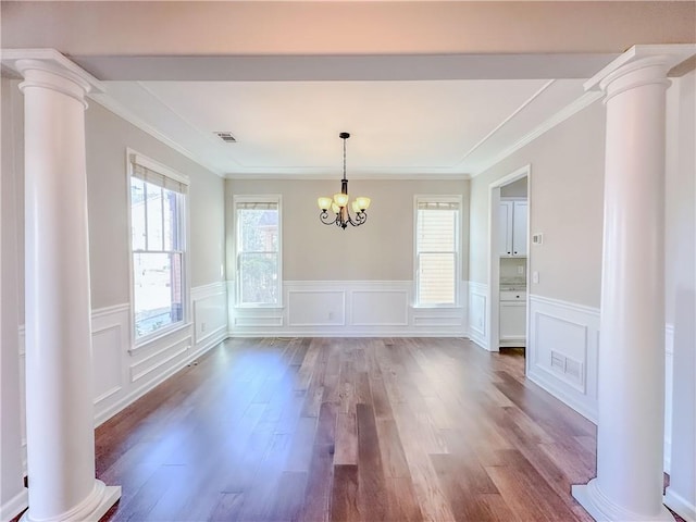 unfurnished dining area featuring wood finished floors, a notable chandelier, a healthy amount of sunlight, and ornate columns