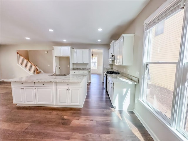 kitchen featuring stainless steel range with gas stovetop, an island with sink, dark wood-style flooring, white cabinets, and a sink