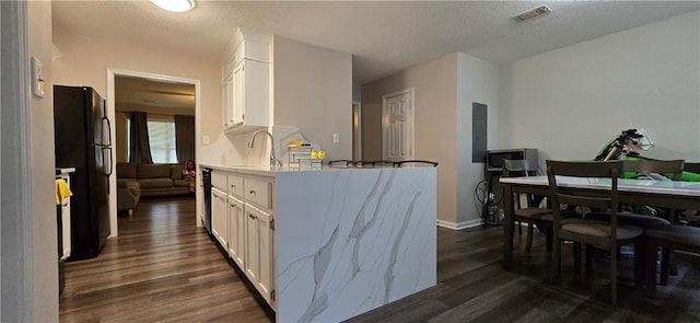 kitchen featuring white cabinetry, kitchen peninsula, dark wood-type flooring, black fridge, and sink