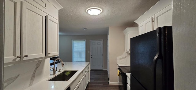 kitchen with white cabinets, black fridge, sink, a textured ceiling, and dark wood-type flooring