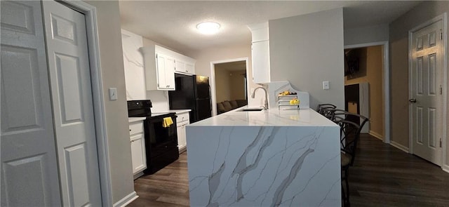 kitchen with white cabinetry, black refrigerator, range, light stone counters, and dark wood-type flooring