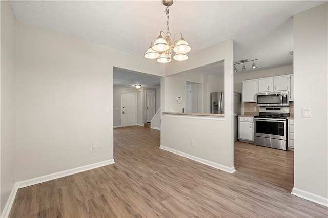 kitchen featuring a notable chandelier, white cabinetry, stainless steel appliances, and light wood-style floors