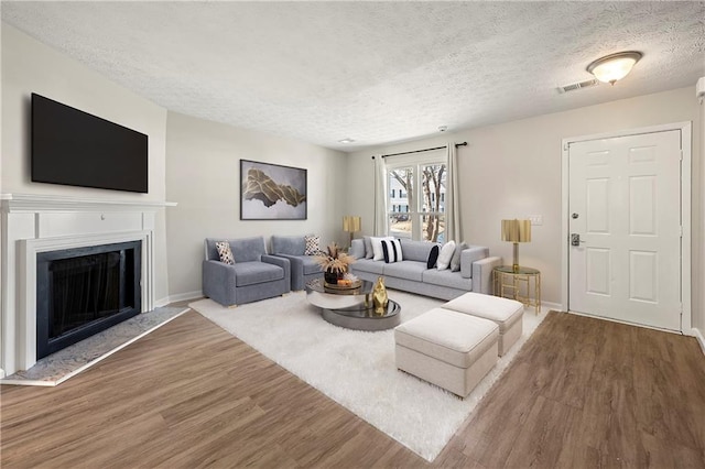 living area with wood finished floors, baseboards, visible vents, a fireplace, and a textured ceiling