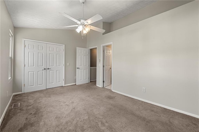 unfurnished bedroom with visible vents, a textured ceiling, a closet, carpet flooring, and lofted ceiling