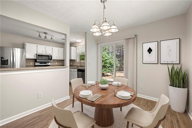 dining area with an inviting chandelier, a textured ceiling, light wood-type flooring, and baseboards