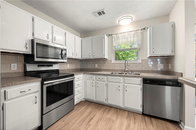 kitchen featuring visible vents, light wood-style flooring, a sink, tasteful backsplash, and stainless steel appliances