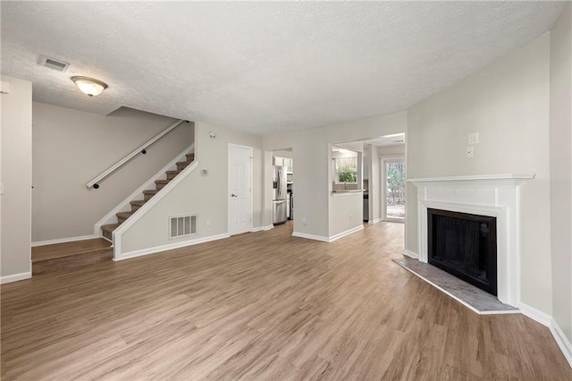 unfurnished living room with visible vents, a fireplace with raised hearth, stairway, and light wood-style floors