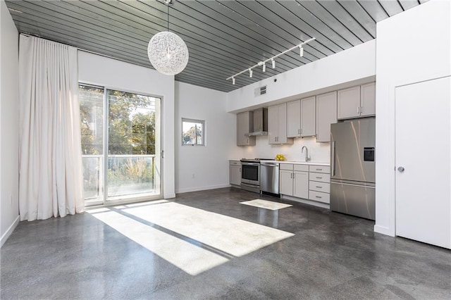 kitchen with a sink, appliances with stainless steel finishes, wall chimney exhaust hood, rail lighting, and baseboards