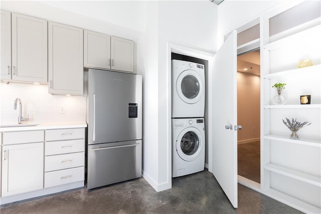 laundry area with a sink, laundry area, baseboards, and stacked washer and dryer