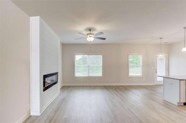 unfurnished living room featuring ceiling fan with notable chandelier, a large fireplace, light hardwood / wood-style floors, and plenty of natural light