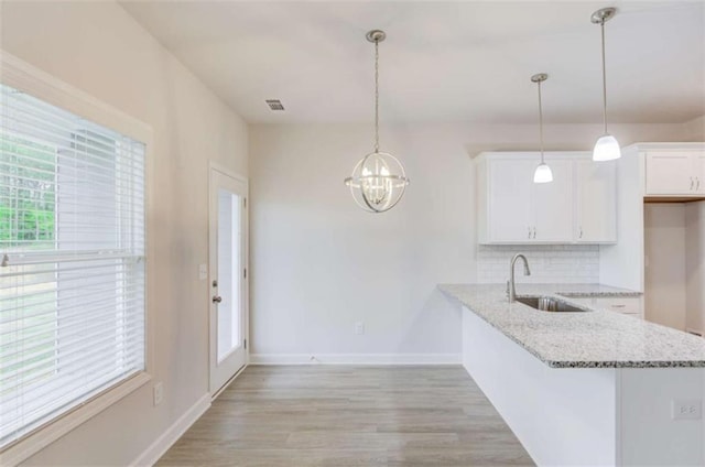 kitchen featuring decorative backsplash, sink, light hardwood / wood-style flooring, white cabinetry, and hanging light fixtures