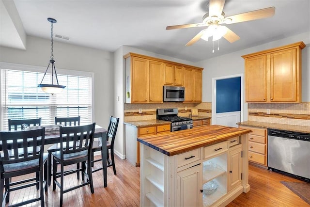 kitchen featuring stainless steel appliances, butcher block countertops, decorative backsplash, a ceiling fan, and light wood-type flooring